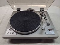 Top view of Akai AP-307 turntable with dust cover open showing platter, tonearm, controls and attached cables