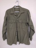 front view of olive green military shirt on hanger