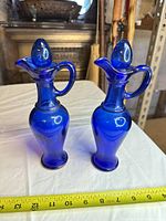 Front view of both cobalt blue glass cruets with stoppers, tape measure for scale