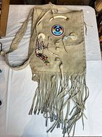 Front view of suede handbag showing bead rosette, fringe, strap