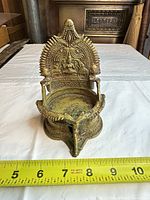 Front view showing ornate arch, deity relief, reservoir bowl and ruler for scale
