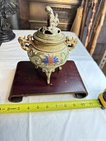 Front view of bronze cloisonné incense burner on wooden stand with tape measure for scale