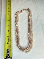 Full view of triple-strand baroque pearl necklace beside ruler showing ~18 inches