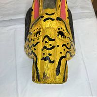 Front view of yellow and black painted wood mask showing eye holes and wear