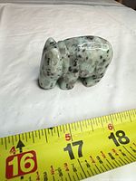 Side view of polished light green stone animal figurine beside tape measure showing length around 2–3 inches