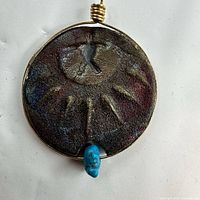 Front view of raku glazed ceramic pendant showing sunburst design, turquoise bead and wire bail