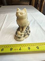 Front view of cream marble cat figurine with ruler indicating height
