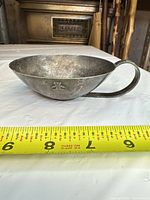 Side view of pewter porringer showing teddy motif and measuring tape indicating length