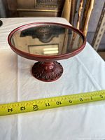 Oblique view of entire red wood pedestal cake stand with tape indicating approx 10 in diameter