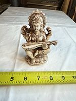 Front view of ivory-tone resin Saraswati figurine beside measuring tape showing about 7 inches height