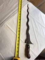 Full view of Kris dagger beside tape showing length