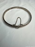 Full view of closed sterling bangle showing round form and safety chain
