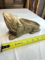 Left side view showing carved foo dog form and tape measure for scale
