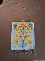 Full view of beaded handbag front showing floral motif, brass frame, chain handle