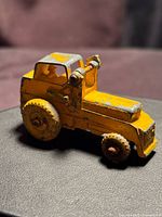 Left side view of yellow die-cast excavator showing chipped paint and missing bucket