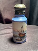 Front view showing blue glass body, hand-painted boat scene, metal lid