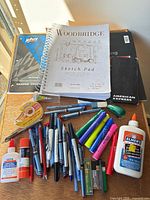 Overview of sketch pads, notebooks, pens, markers, glue and accessories on table