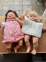 Both dolls laid side by side with bib and blanket visible