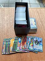 Stack of cards inside black storage box with spread of Dragon Ball Super cards in front