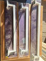 Three packaged white towel bars laid side by side