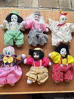 Group shot of all six porcelain-head clown dolls laid out on tabletop