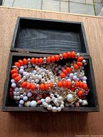 Necklaces stored inside open wooden jewelry box showing orange and pearl strands