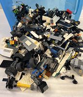 Large pile of mixed LEGO pieces in blue bin showing variety of brick types and vehicle parts