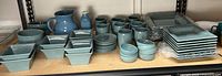 Full shelf view showing entire blue stoneware dinnerware set, pitcher and milk bottle