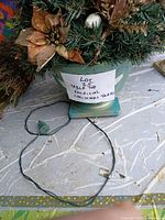 Turquoise planter base with artificial evergreen tree, visible string light cord and plug