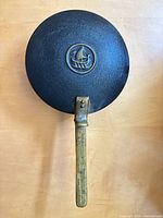Underside of skillet showing brass handle and ship logo