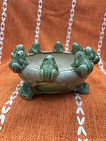 Top angled view of small green ceramic planter with ring of frog figurines