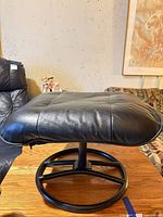 Front view of black leather ottoman on round metal base