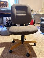 Front view of gray fabric desk chair showing seat, backrest, wood base and casters