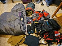 Group shot of backpacks, sleeping bags, water shoes, hydration bladder and towels on floor