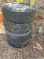 Three of the four mounted tire and wheel assemblies stacked outdoors, showing tread pattern and wheel style