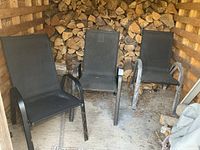 Three black mesh metal deck chairs standing upright in storage area