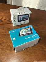 Garmin Drive 50 and TomTom VIA 1535TM GPS units in their original boxes on tabletop