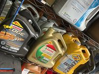 Shelf with multiple jugs: Castrol Edge black jug, Castrol Edge green jug, two Pennzoil Platinum yellow jugs, additional grey jugs behind