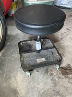 Full view of metal rolling stool showing black padded seat, metal base, and casters