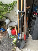 Group of four long-handled yard tools including serrated Sabretooth shovel, pointed D-handle shovel, post-hole shovel, and log roller