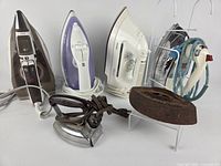 Group showing six electric irons, one cast iron sad iron, wall rack