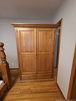 Front view of closed oak armoire showing doors, knobs, drawers, crown molding
