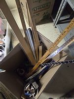 Open box containing assorted measuring tools such as yardsticks, straight edges, triangles, tape roll