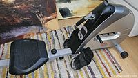 Right side profile of Sunny Health & Fitness rowing machine showing frame, seat, footplates and wheels