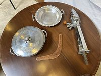 Group shot of all four items: hammered aluminum casserole with lid, matching serving bowl, chrome beer tap tower, wooden boomerang
