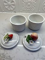Two open white ceramic jars and two lids with strawberry and peach motifs
