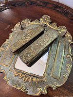 Wall-mount brass mirror plaque with two matching brushes displayed on wooden surface