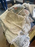 Pile of assorted textiles including crochet cover, tapestry pillow cover, embroidered white linens