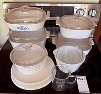 Assorted CorningWare dishes stacked on stovetop with lids and measuring beaker visible