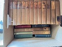 Open box showing matched set of 15 brown cloth volumes and additional assorted hardcovers beneath